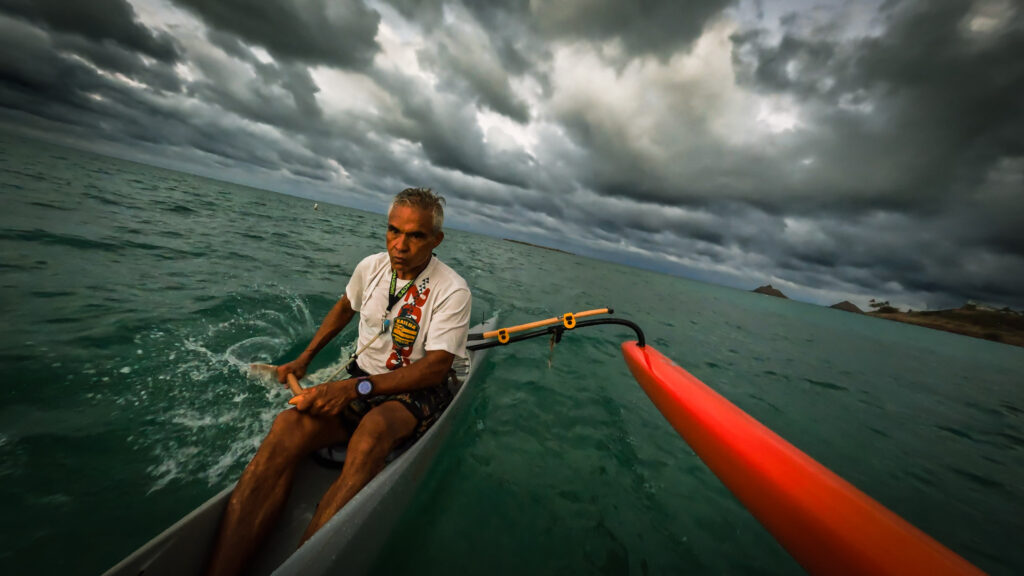 Man paddling a small boat on a cloudy ocean.